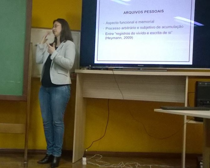 A imagem mostra a bibliotecária Vania da Costa apresentando sua dissertação