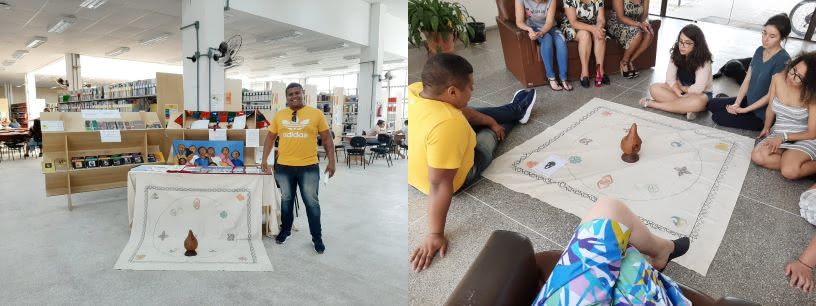 Montagem com duas fotos: a primeira aparece o acervo da biblioteca ao fundo a frente uma mesa com uma toalha, ao centro um objeto que lembra uma cuia. A direita da foto o palestrante que usa calça jeans camiset amarela, oculos pendurado no pescoço e expressa sorriso. Na foto da direita uma toalha colocada no cão com um objeto ao centro que lembra uma cuia, ao redor pessoas sentadas no chão outras sentadas em sofas posicionados ao redor dessa toalha.