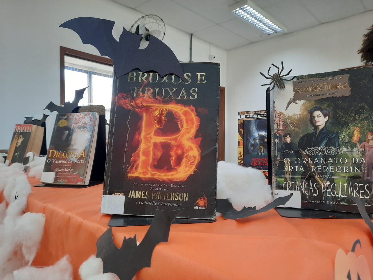 Imagem com fundo na cor laranja e livros que tratam sobre o tema da exposição halloween