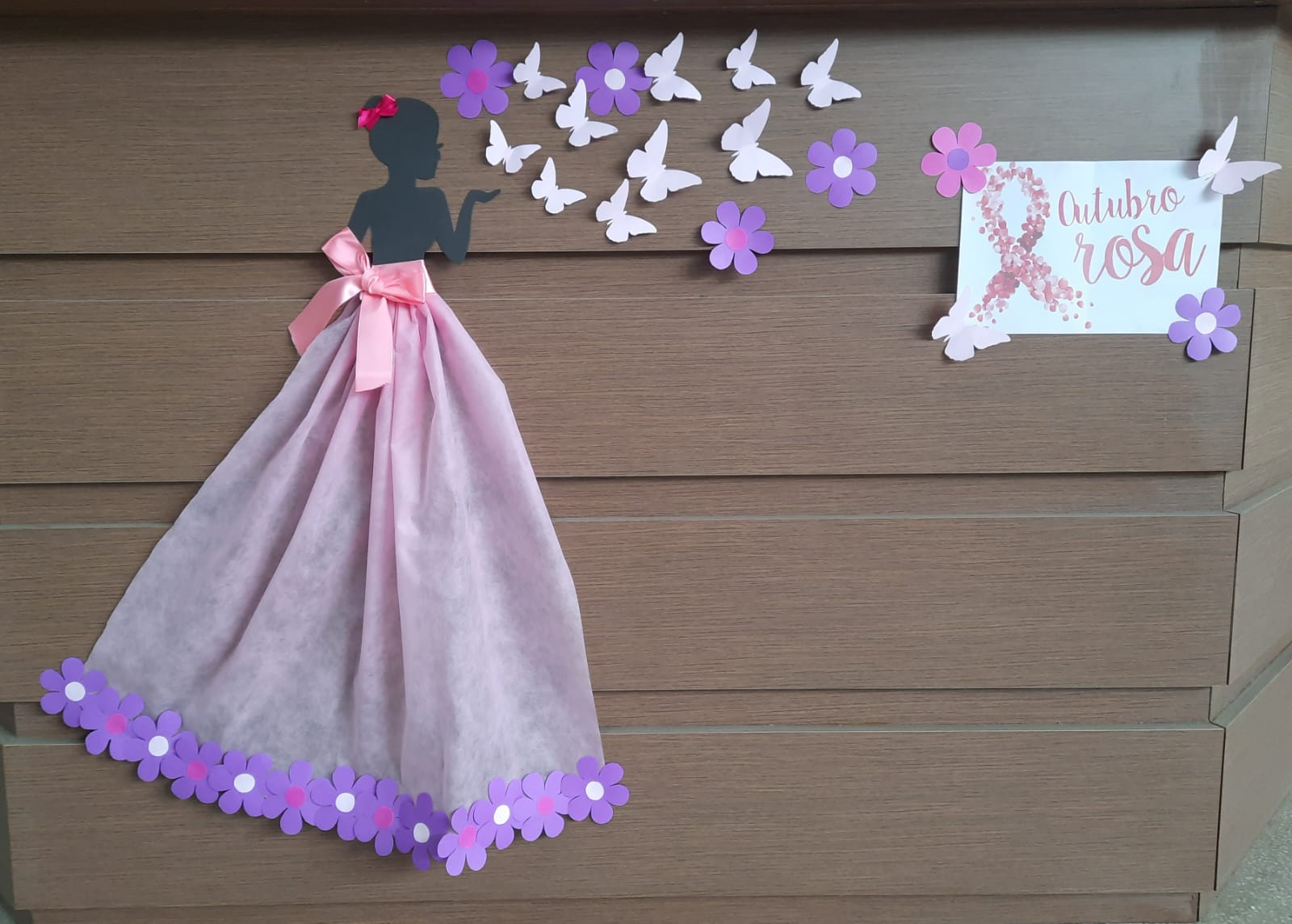 Imagem fundo marrom com uma moça de vestido rosa com flores na barra e borboletas voando.