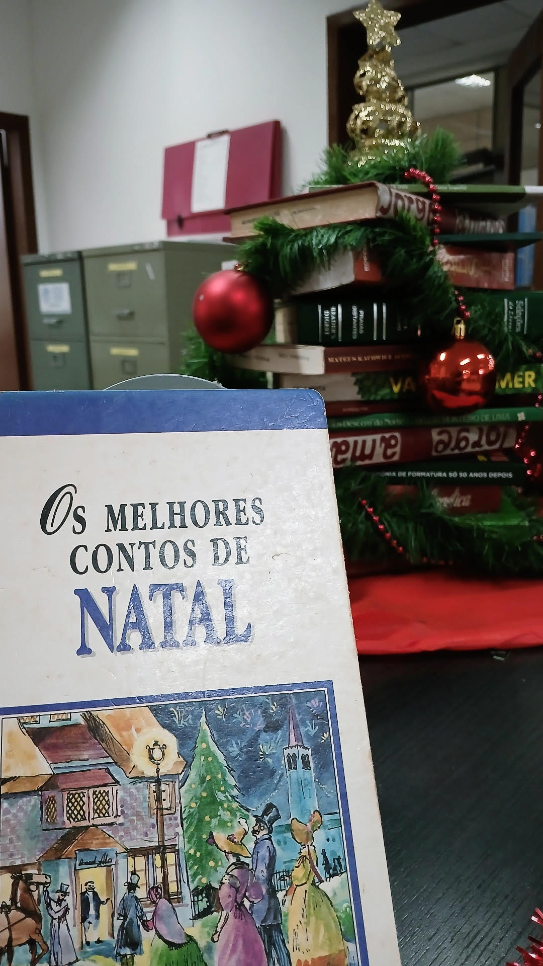 Imagem da exposição de Natal, com a capa do livro "Os melhores contos de natal" a frente e atrás uma árvore de livros pequena.