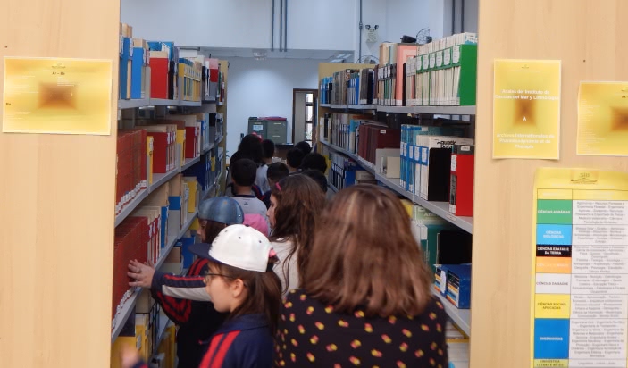 alunos entre duas estantes de livros, observando atentos os livros
