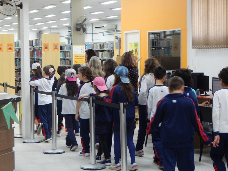 alunos entrando na biblioteca em fila, usando bones, camisetas brancas, e calças azul escuro